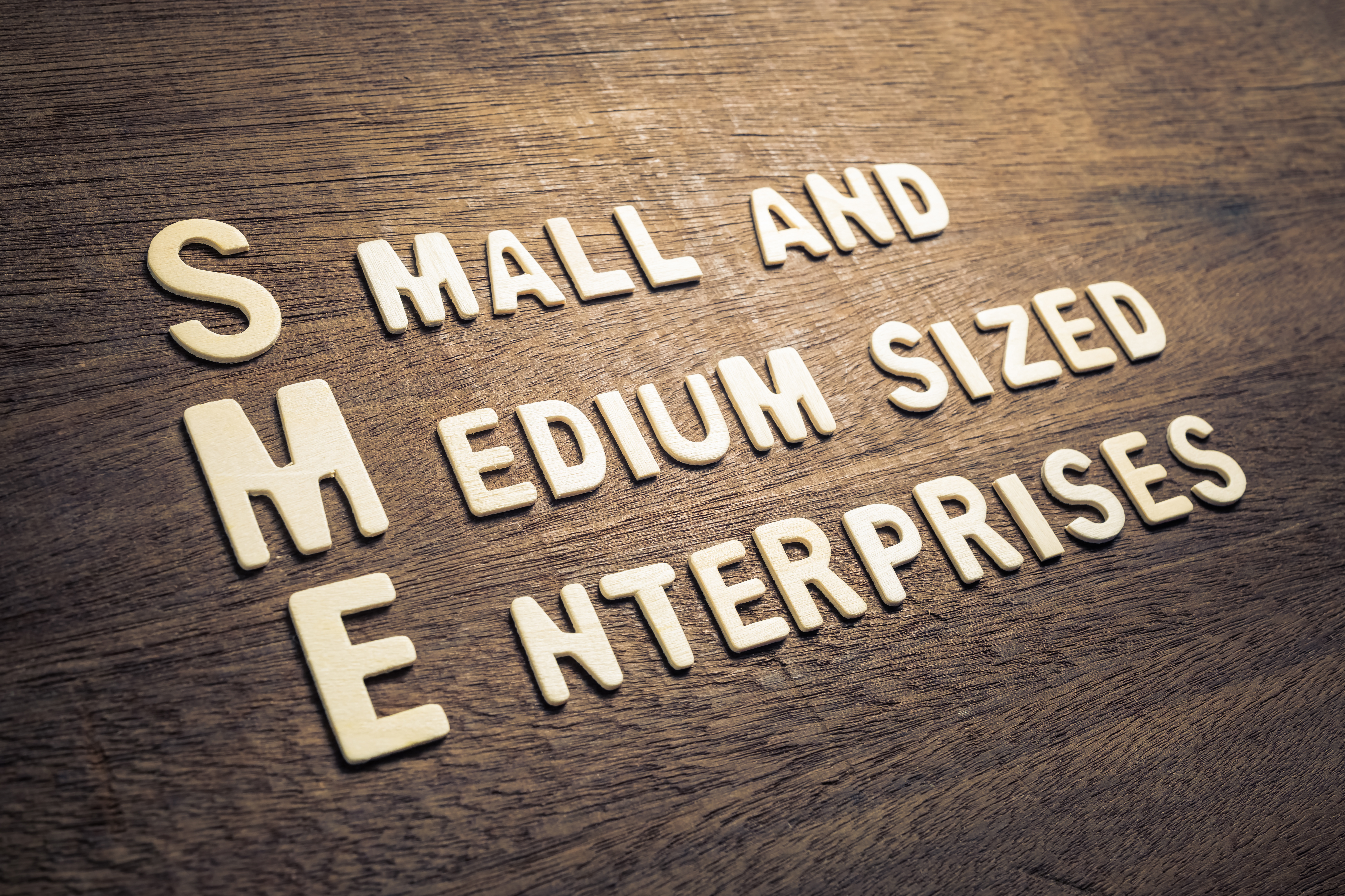 SME Small and medium sized enterprises. Bokstäver av trä mot träbakgrund